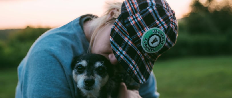 person hugging and kissing dog in a field with pink sunset