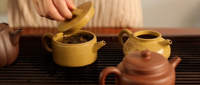 A hand lifting the lid off a teapot, revealing tea inside