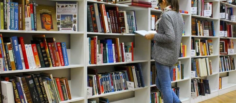 Menina na biblioteca pesquisando sobre faculdades com curso gratuito