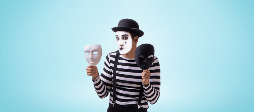 A mime with white face makeup and black fake teardrop holding a white mask and a black mask in each