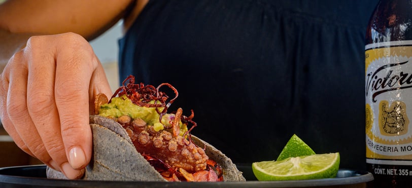 a person holding a taco in a plate by Drai Cabello in Cancun