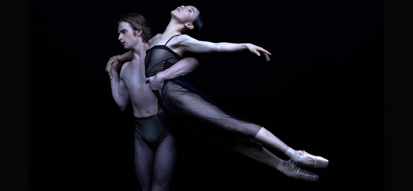 Two ballet dancers perform a dramatic lift against a black background.