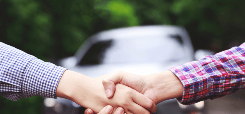 two people shaking hands with a car in the background