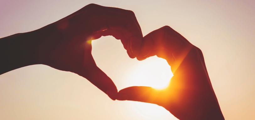 a person making a heart shaped with her hands in the sunset
