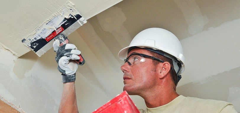 man using drywall knife to apply mud