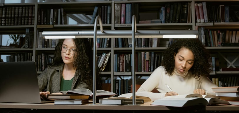 two women sitting at a table with books and a laptop
