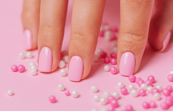 a hand with pink nail paint and some pearls