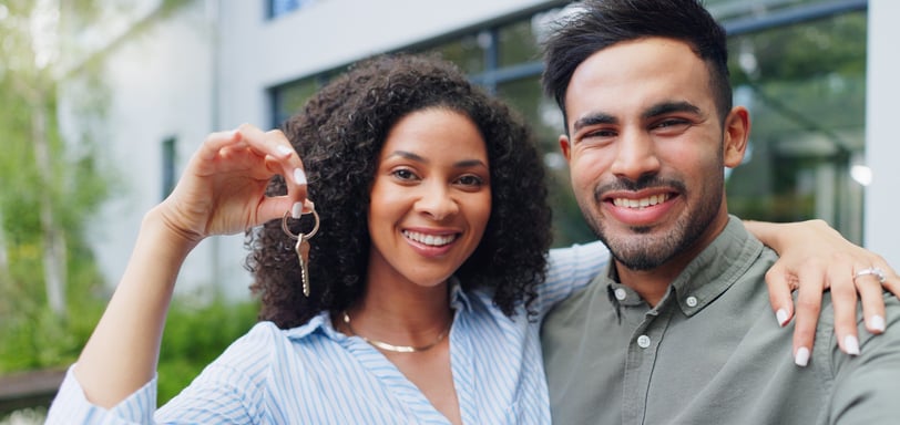 A happy family holding house keys in front of a new home.