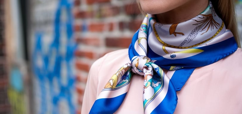 A photo of a woman wearing a printed silk scarf. The scarf is wrapped around her neck and tied with a bow at the front