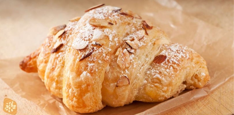 Golden almond croissant topped with sliced almonds and powdered sugar, resting on parchment paper