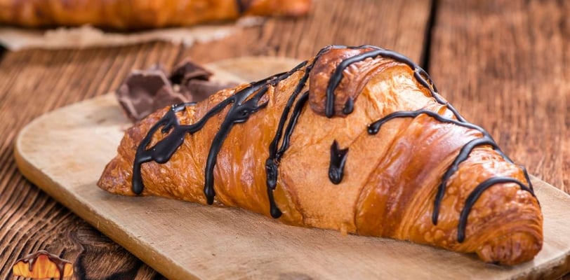 Freshly baked croissant drizzled with rich chocolate on a rustic wooden board