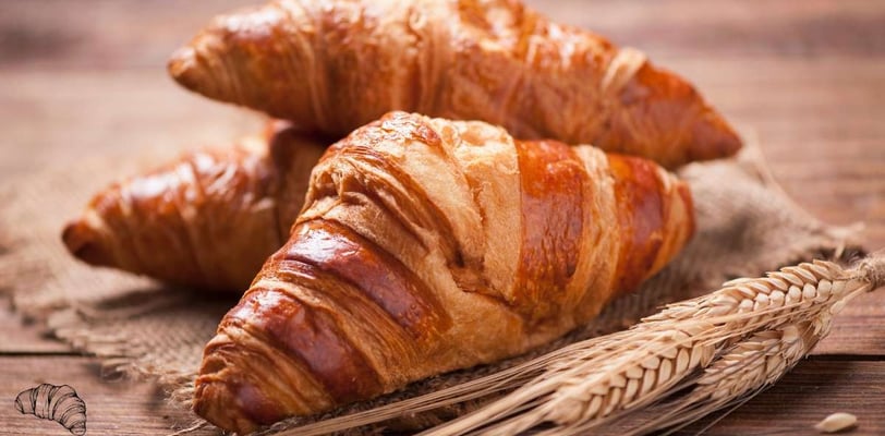 Freshly baked croissant along with wheat grains on a rustic wooden board