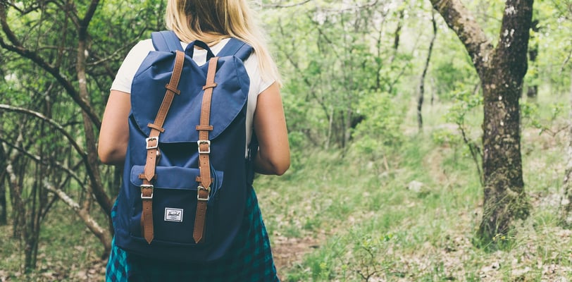 a woman in a blue dress and backpack on a trail