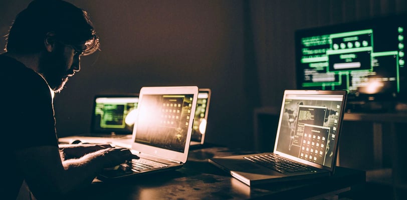a man sitting at a desk with two laptops
