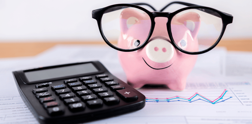 piggy bank holding glasses on financial paperwork next to a calculator