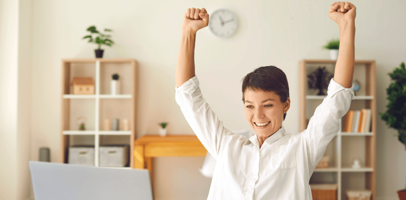 a very happy woman sitting at a desk with her arms up in the air