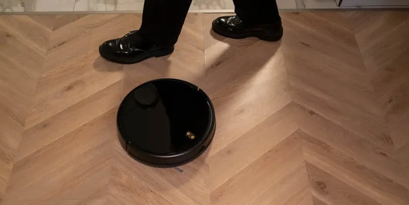 a person standing on a wooden floor with a robot vacuum