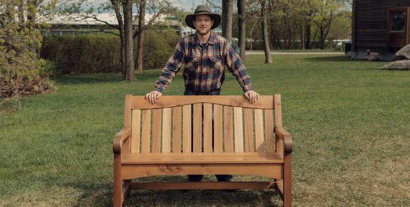a man in a hat and plaid shirt standing in front of a bench