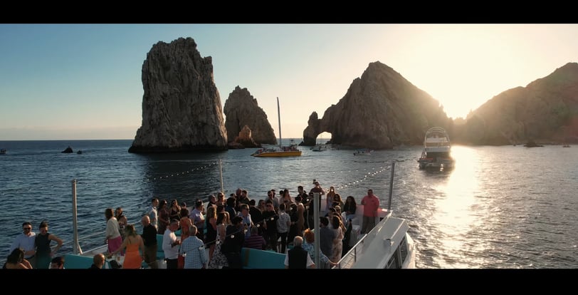 Captured moment of a pre-wedding gathering on a boat with the Cabo San Lucas arch visible in the background. Filmed for Weddi
