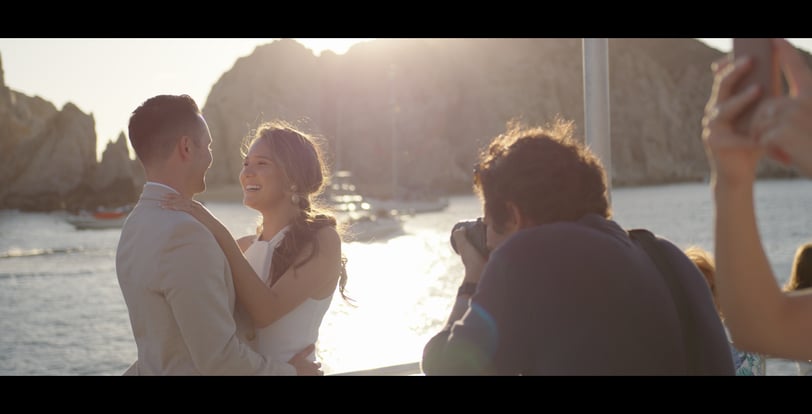 Photographer capturing images of a couple with the sea and yachts in the background, bathed in golden light; scene taken from
