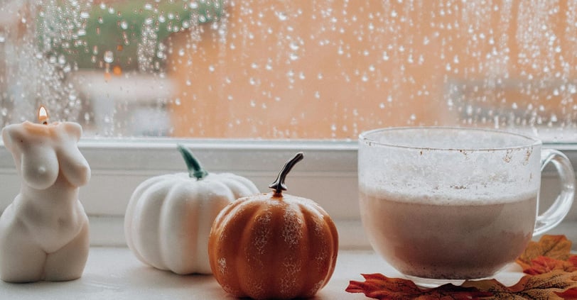 Cozy living: A window sill with pumpkin latte, candlelight, autumn decor, and raindrops on glass.