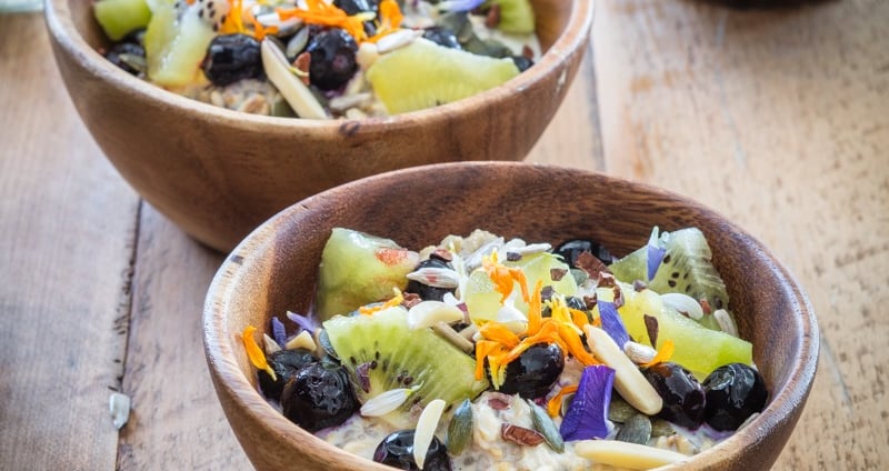 two wooden bowls of oaty chia coconut with fruit and nuts on a table