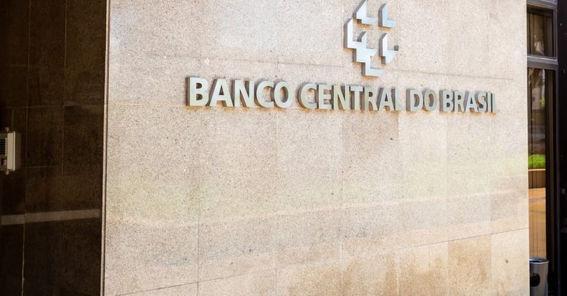 Fachada do Banco Central do Brasil, com logotipo metálico e parede de pedra clara, em perspectiva