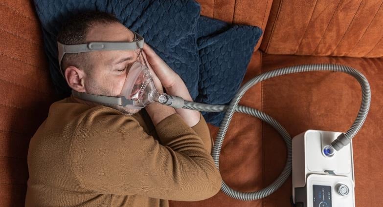 a man sleeping on a couch with a mask using cpap machine for sleep apnea