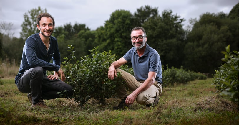 two men sitting on a field with trees in the background