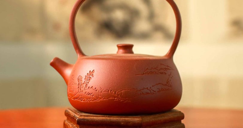 A brown teapot with carved artwork placed on a wooden stand