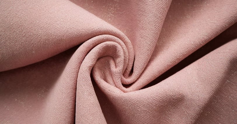 A close-up shot of a recycled polyester material. The material is a soft pink hue and has a subtle texture
