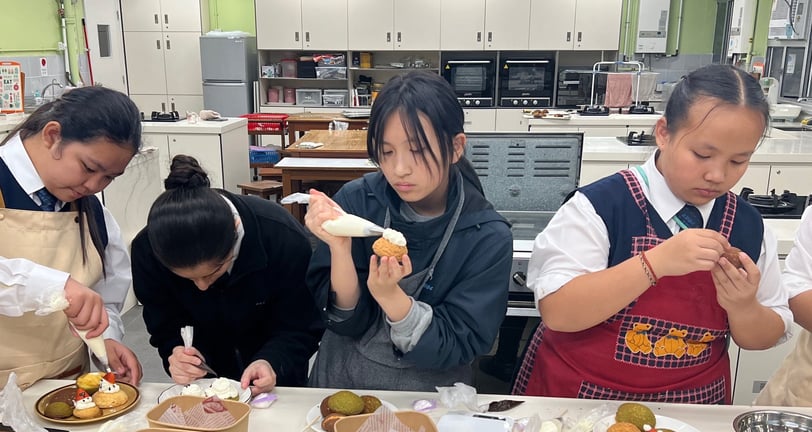 同學們喺設備齊全嘅廚房中專注裝飾甜點,使用唧花袋為 泡芙加上糖霜和士多啤梨裝飾,營造出互動學習嘅熱鬧氛圍