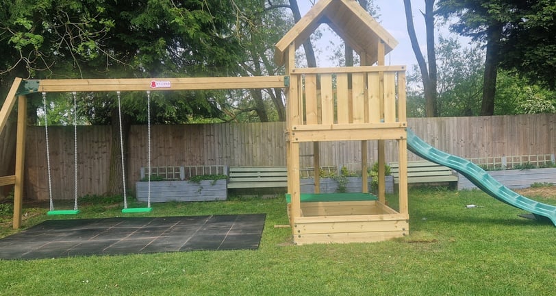 a wooden swing set with a slide in a beer garden