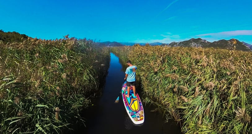 a man is standing on a paddle board in narrow chanel