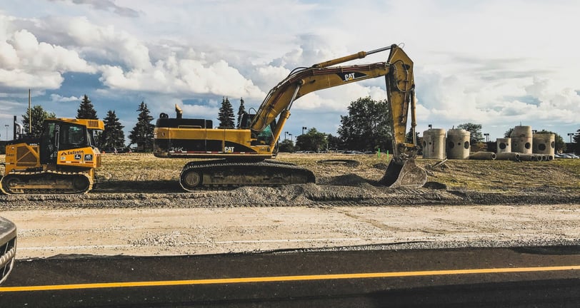 Escavadeira e maquinário pesado em um canteiro de obras, preparando o terreno para construção sob um céu azul com nuvens.