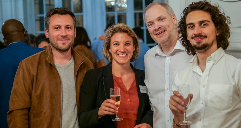 Trois hommes et une femmes qui sourient avec des coupes de champagne dans les mains
