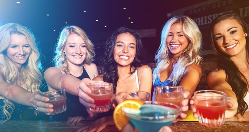 Group of smiling women toasting cocktails across the bar during a girls’ night out in downtown Las Vegas.