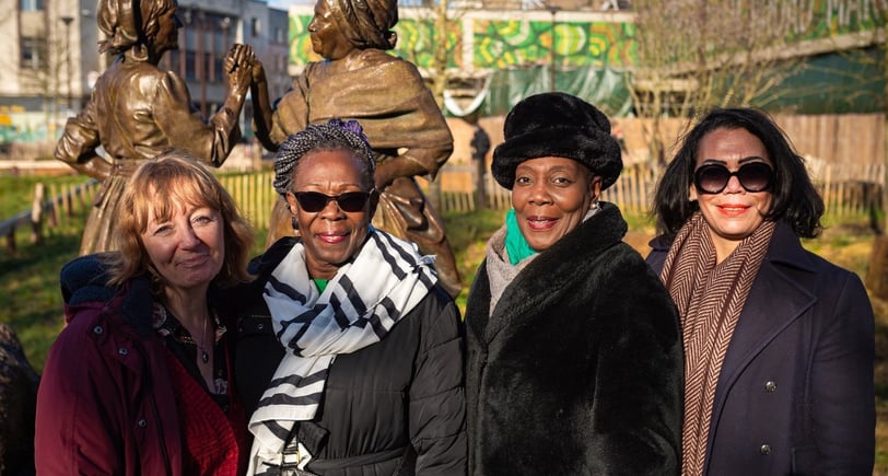 a group of women standing in front of a statue of a man