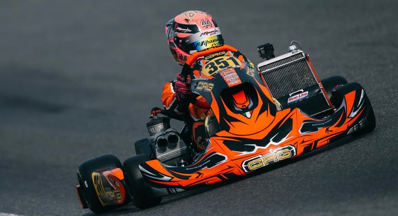 Pilote de karting en tenue orange sur le kart numéro 351 en pleine course.