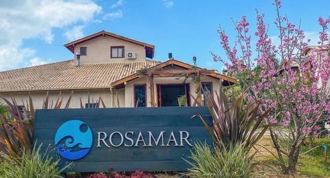 Casa grande com vegetações da volta e uma placa na frente com o novo logo do Hostel Rosamar