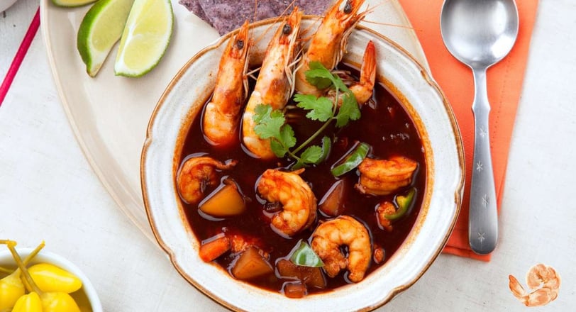 Caldo de Camaron in a bowl, featuring shrimp in a rich red broth, garnished with cilantro and served with lime wedges