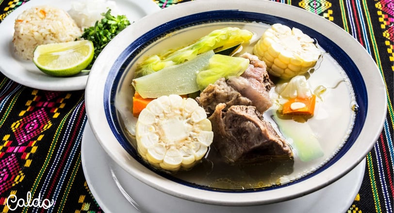 Traditional caldo de res served in a bowl with tender beef, fresh vegetables, corn, and sides of ric