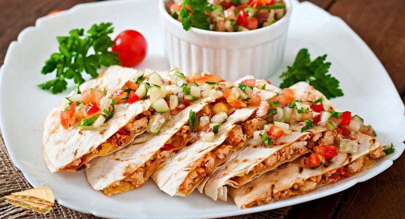 Chicken quesadilla slices garnished with fresh pico de gallo on a white plate, served with tomatoes and parsley as garnish