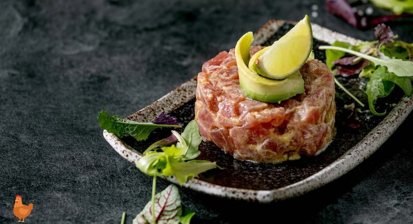 chicken tartare dish topped with avocado slices and lime, served with fresh mixed greens