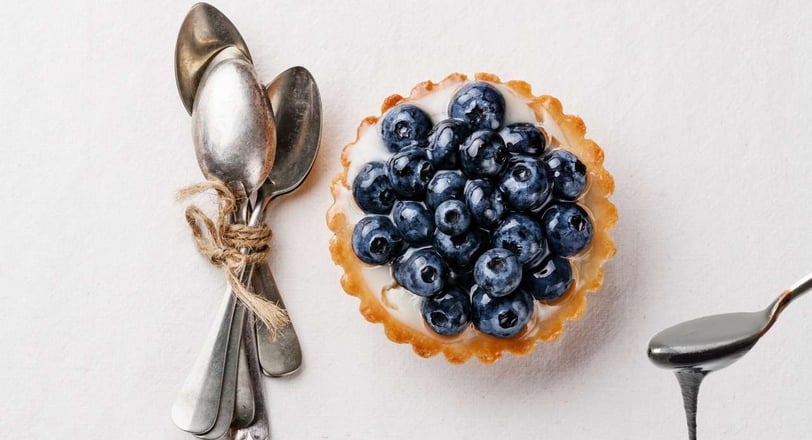 Elegant arrangement of vintage dessert spoons tied with twine, placed beside a blueberry tart with creamy filling