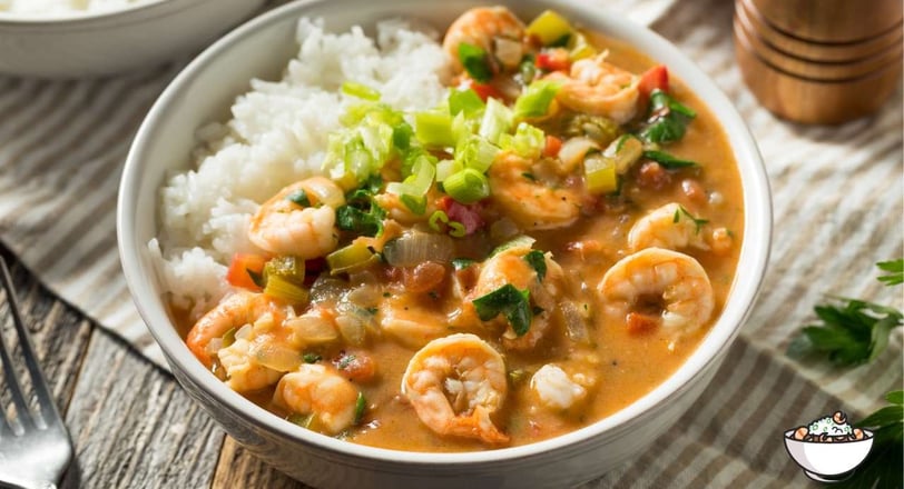 A bowl of Gumbo with shrimp, rice, and green onion garnish in a white bowl