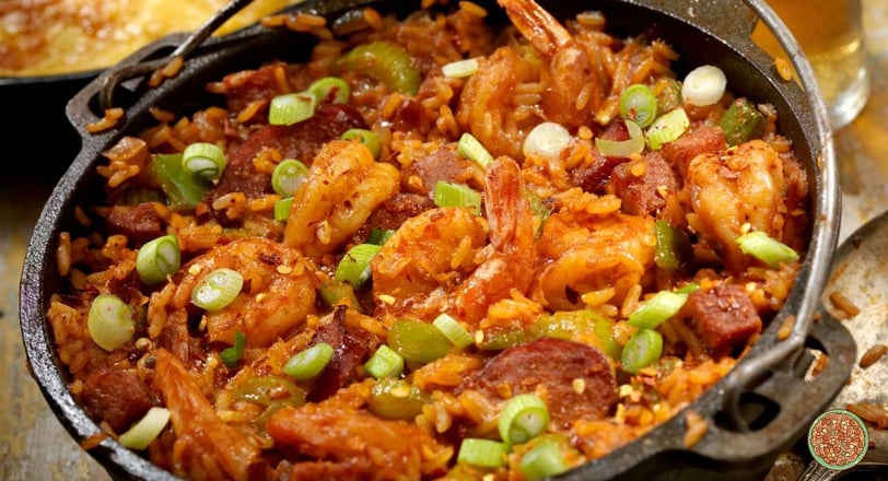 A rustic skillet filled with spicy Jambalaya, featuring seasoned rice, juicy shrimp, slices of sausage, and fresh green onion