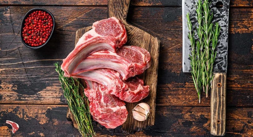 Raw mutton chops with rosemary, garlic, and red peppercorns on a wooden board