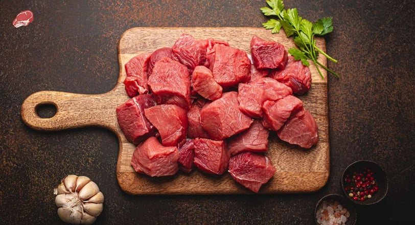 diced mutton pieces on a wooden cutting board, along with parsley, a garlic, peppercorns and Himalayan salt