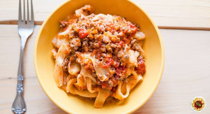 Pappardelle pasta topped with a rich and hearty Bolognese sauce served in a yellow bowl, perfect for authentic Italian dinner